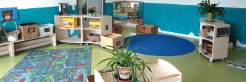 Das Türkisene Zimmer mit Spielteppich, Regalen und Kisten mit Spielzeug